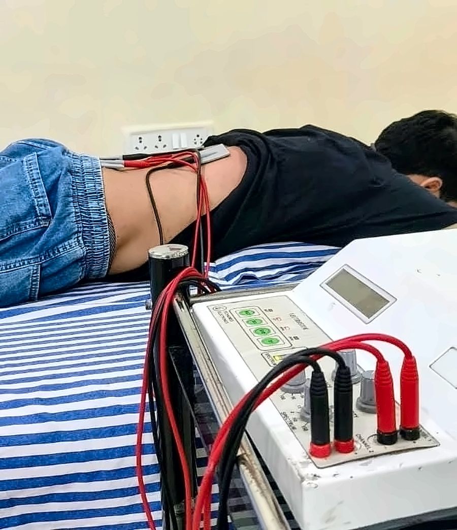 Electrotherapy pads on the lower back of a patient lying face down, connected to an IFT and TENS unit, for back and lower back pain at MuvAgain Physiotherapy Patna
